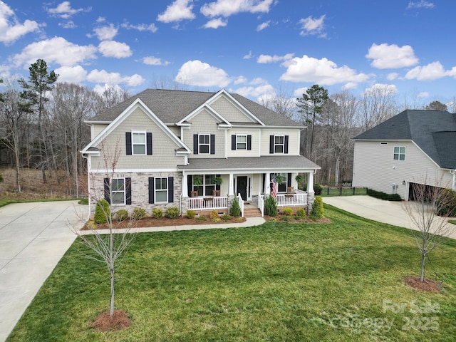 view of front of property with a front yard, a porch, a shingled roof, concrete driveway, and stone siding