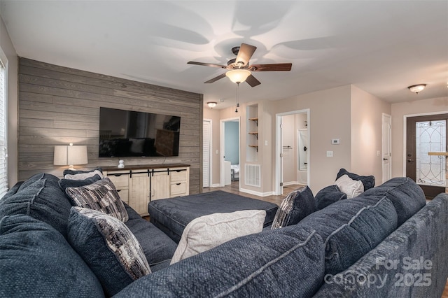 living room with visible vents, wooden walls, an accent wall, ceiling fan, and baseboards