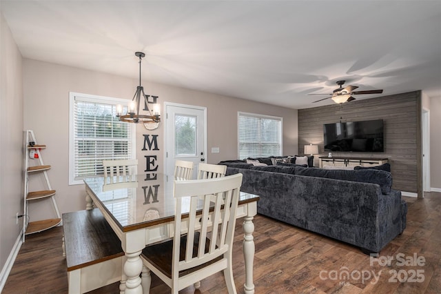 dining room with dark wood-type flooring, ceiling fan with notable chandelier, and baseboards