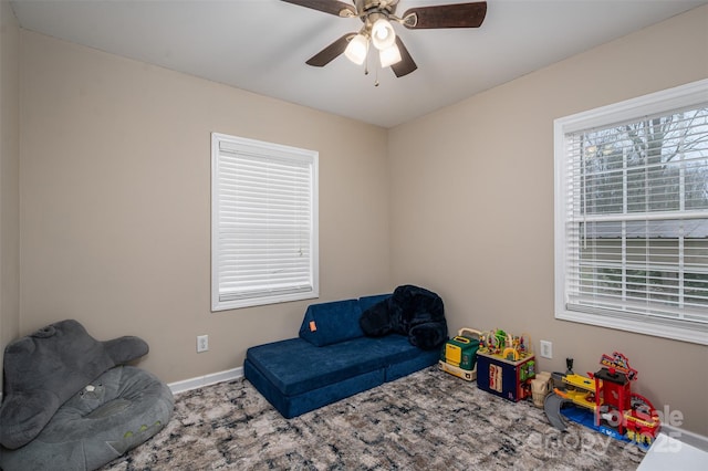 living area with a healthy amount of sunlight, a ceiling fan, and baseboards