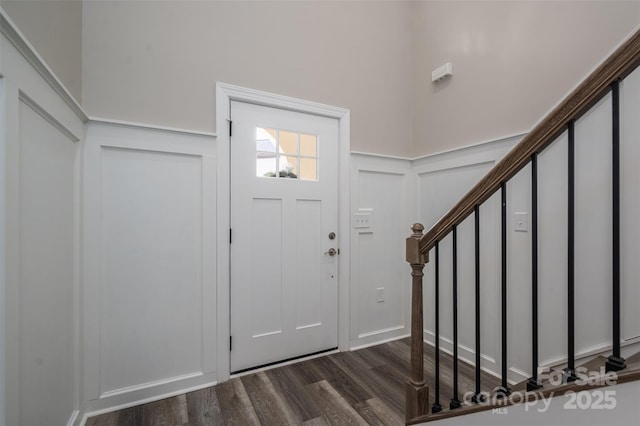 foyer entrance with stairway, dark wood finished floors, wainscoting, and a decorative wall