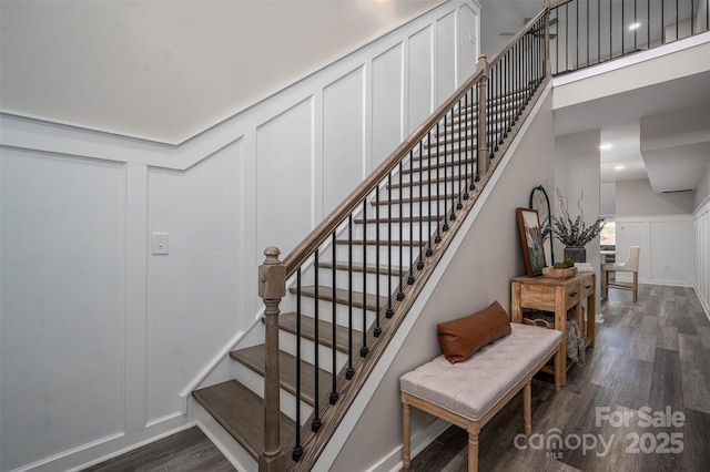 staircase with a decorative wall, a high ceiling, and wood finished floors