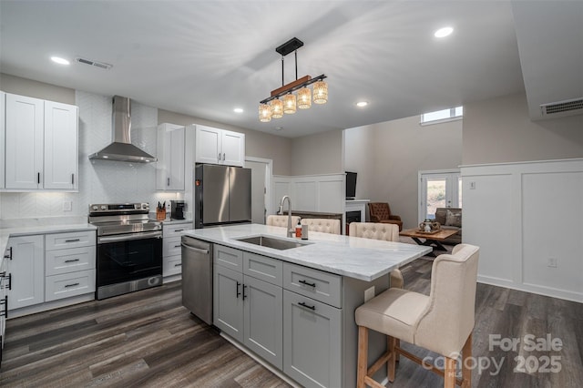 kitchen with dark wood-type flooring, a breakfast bar, appliances with stainless steel finishes, wall chimney exhaust hood, and a sink