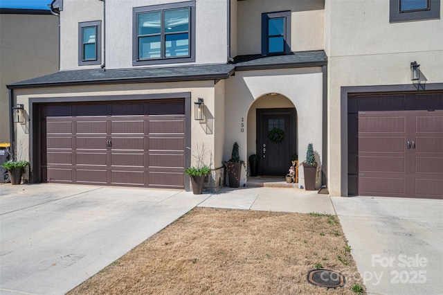 entrance to property with stucco siding, driveway, and a garage