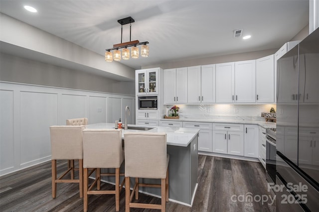 kitchen featuring a sink, a breakfast bar area, appliances with stainless steel finishes, white cabinetry, and dark wood-style flooring