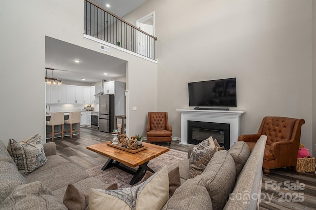 living room featuring dark wood finished floors, a glass covered fireplace, recessed lighting, and visible vents