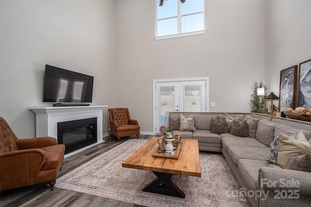 living room with a glass covered fireplace, wood finished floors, french doors, a high ceiling, and baseboards