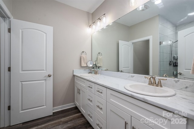 bathroom with double vanity, a shower stall, wood finished floors, and a sink