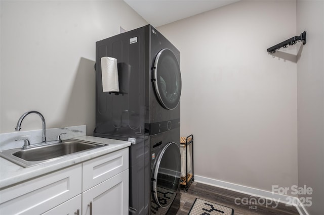 laundry room with a sink, dark wood-style floors, cabinet space, stacked washer / dryer, and baseboards