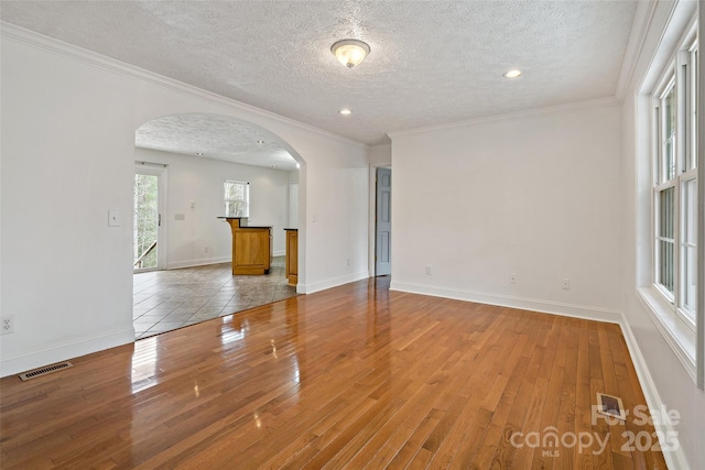 empty room featuring visible vents, arched walkways, wood-type flooring, and crown molding