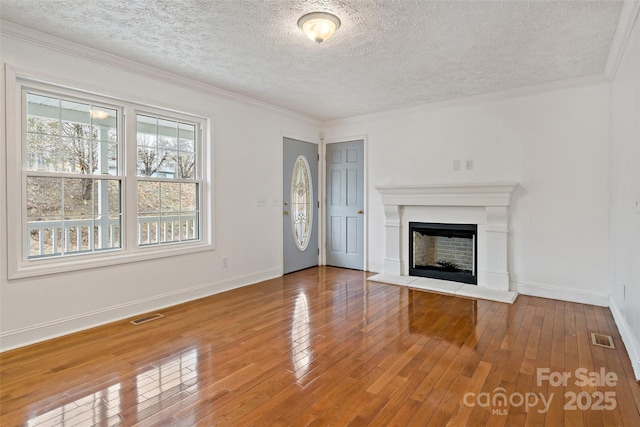 unfurnished living room featuring visible vents, baseboards, a fireplace with raised hearth, and hardwood / wood-style flooring