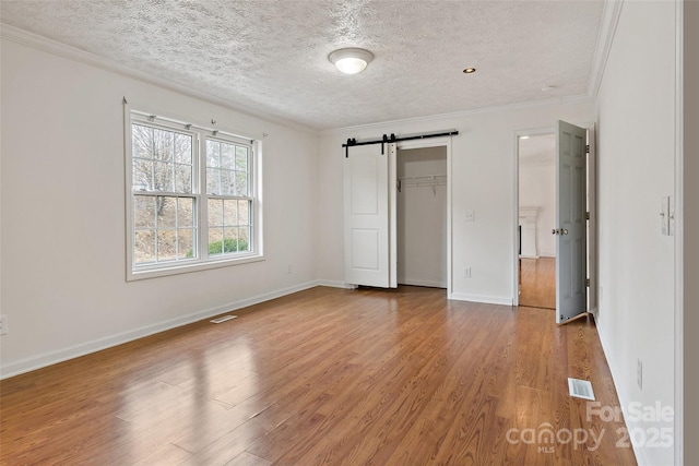 unfurnished bedroom featuring visible vents, a barn door, wood finished floors, and crown molding