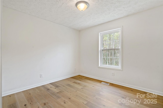 empty room featuring a textured ceiling, baseboards, visible vents, and light wood-type flooring