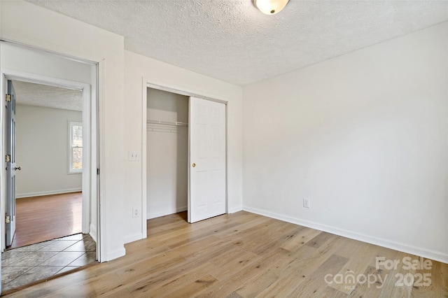 unfurnished bedroom featuring light wood-type flooring, baseboards, a textured ceiling, and a closet