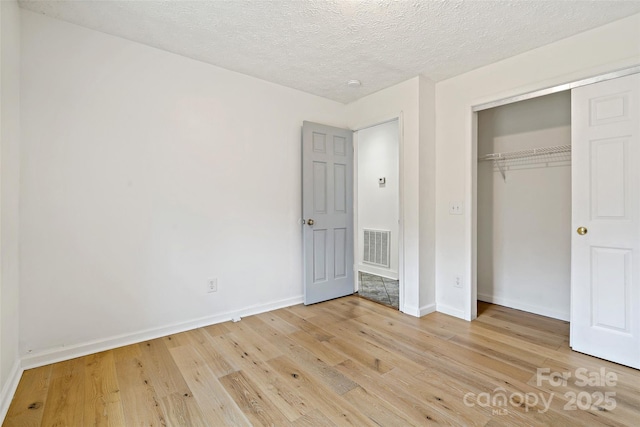 unfurnished bedroom featuring visible vents, baseboards, light wood-type flooring, a closet, and a textured ceiling