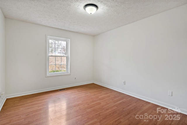 unfurnished room featuring a textured ceiling, baseboards, visible vents, and light wood-type flooring