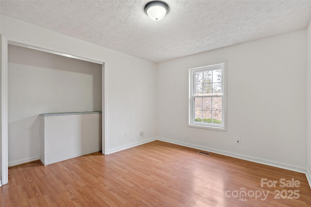 empty room featuring light wood-style flooring, a textured ceiling, and baseboards