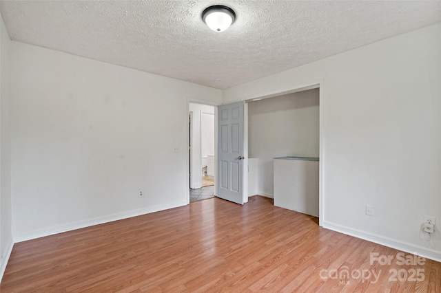 spare room with baseboards, light wood-style floors, and a textured ceiling