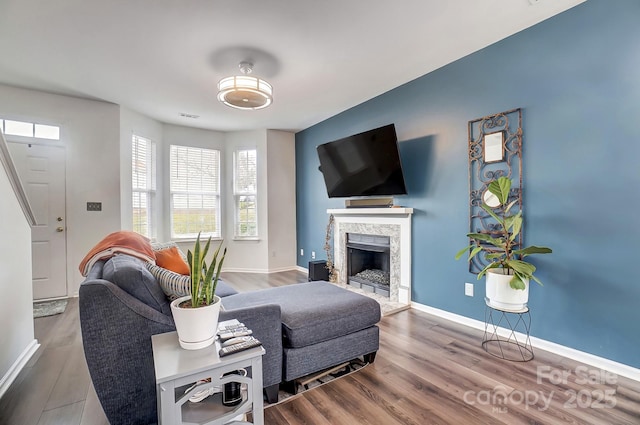 living room with visible vents, baseboards, a fireplace with raised hearth, and wood finished floors