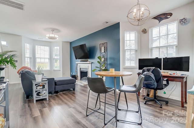 home office featuring a notable chandelier, visible vents, a fireplace, and wood finished floors