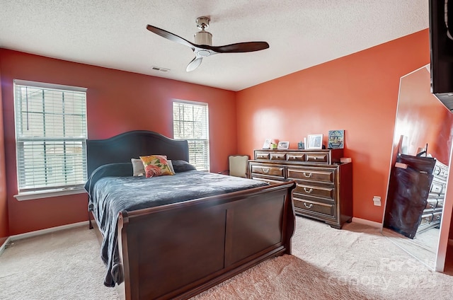 bedroom with a ceiling fan, light colored carpet, visible vents, and a textured ceiling