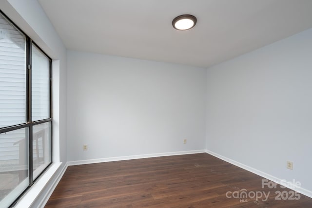 empty room with dark wood finished floors, plenty of natural light, and baseboards