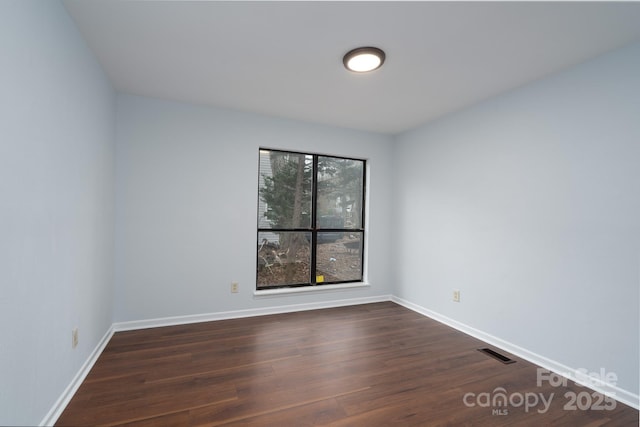 spare room featuring visible vents, baseboards, and dark wood-style flooring