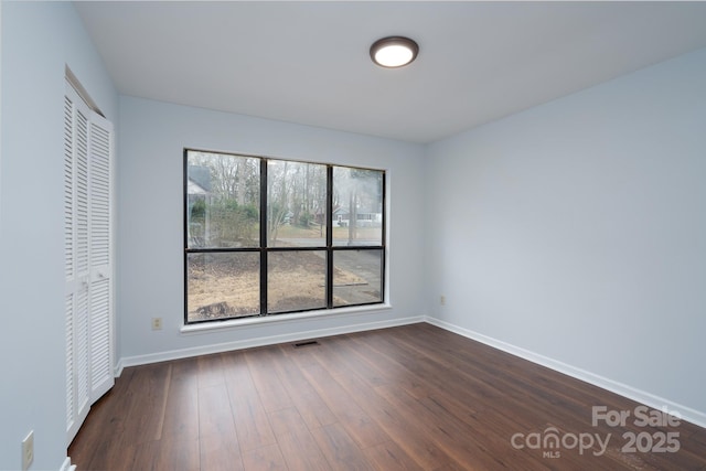 unfurnished bedroom with dark wood finished floors, baseboards, visible vents, and a closet