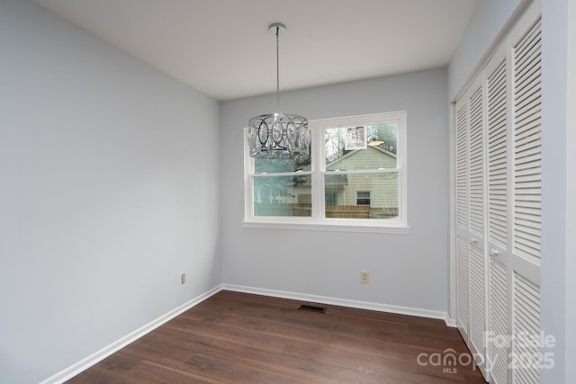 unfurnished dining area with visible vents, baseboards, a notable chandelier, and dark wood-style floors