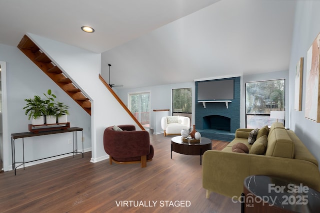 living area featuring wood finished floors, a fireplace, lofted ceiling, ceiling fan, and stairs