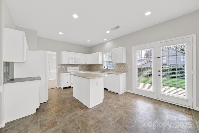 kitchen with visible vents, a sink, a center island, white appliances, and decorative backsplash