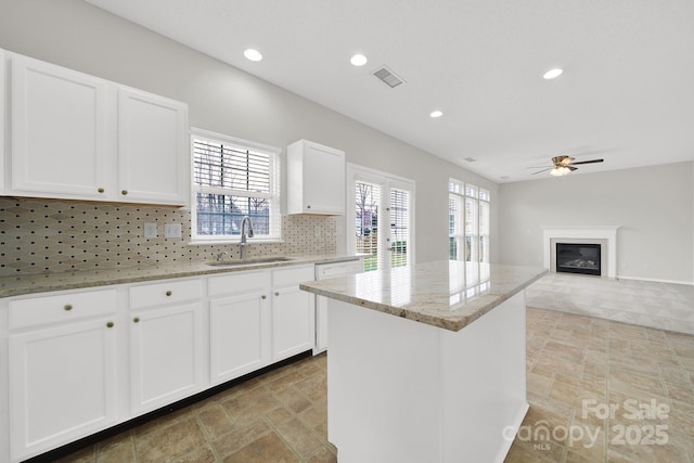 kitchen with light stone counters, a ceiling fan, visible vents, a sink, and backsplash