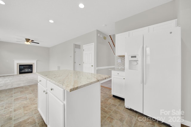 kitchen with a ceiling fan, stone finish floor, light stone counters, a kitchen island, and white fridge with ice dispenser