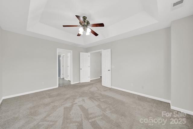 empty room with a tray ceiling, a ceiling fan, and baseboards