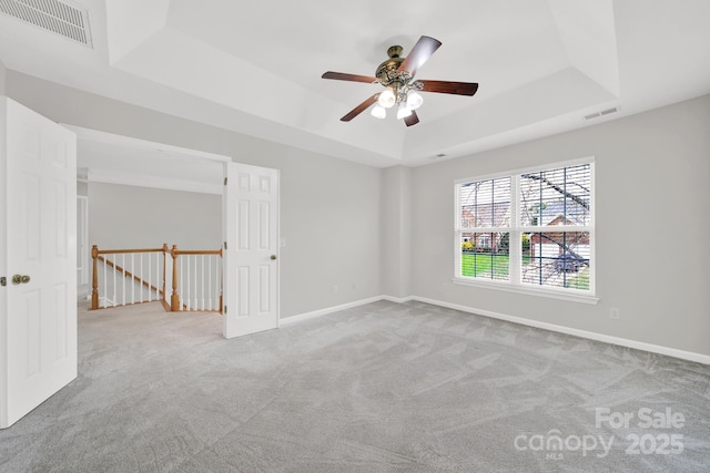 carpeted spare room with visible vents, a raised ceiling, and baseboards