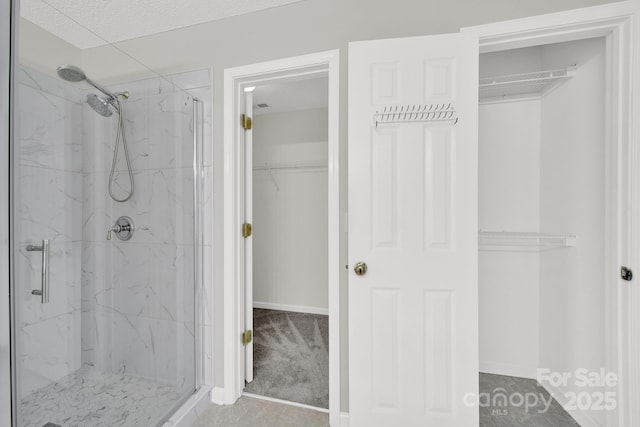 bathroom featuring a walk in closet, baseboards, and a marble finish shower