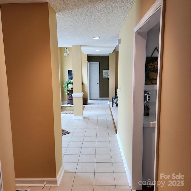 hallway with light tile patterned floors, a textured ceiling, and baseboards