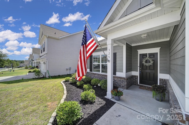 view of exterior entry with a porch, a yard, and brick siding