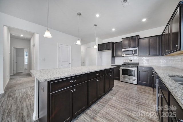 kitchen with light wood-style flooring, light stone counters, tasteful backsplash, and appliances with stainless steel finishes