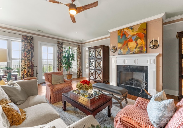 living room featuring baseboards, a fireplace, a ceiling fan, and crown molding