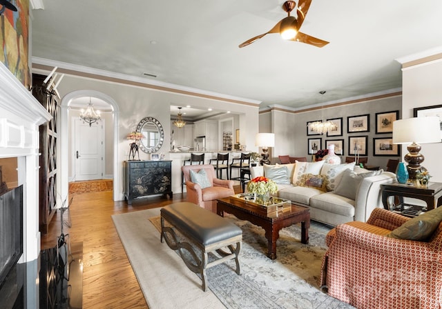 living area featuring visible vents, light wood-type flooring, ornamental molding, ceiling fan with notable chandelier, and a fireplace