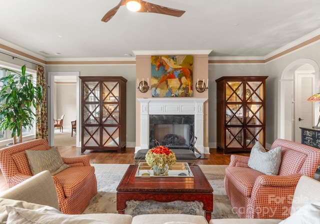 living room with a high end fireplace, ornamental molding, ceiling fan, and wood finished floors