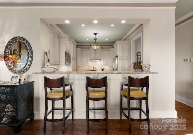 kitchen with a peninsula, light stone countertops, dark wood-style flooring, and appliances with stainless steel finishes