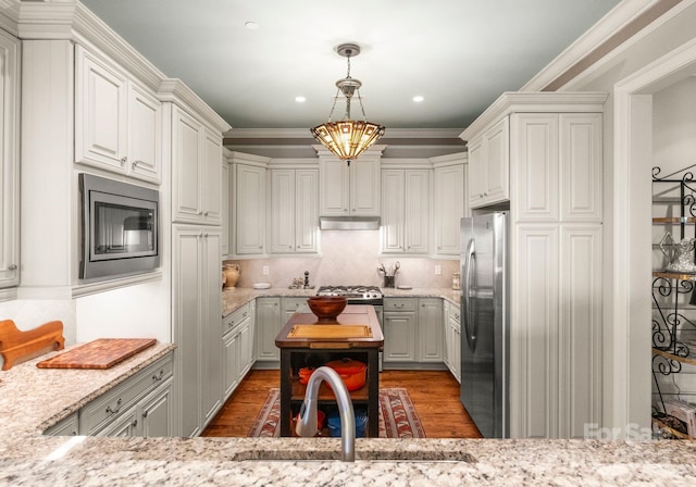 kitchen featuring backsplash, under cabinet range hood, appliances with stainless steel finishes, wood finished floors, and a sink