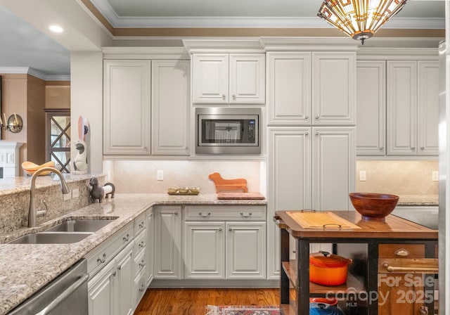 kitchen with wood finished floors, ornamental molding, a sink, white cabinets, and appliances with stainless steel finishes