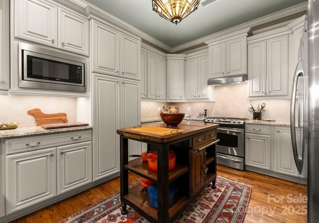 kitchen featuring under cabinet range hood, decorative backsplash, appliances with stainless steel finishes, wood finished floors, and white cabinets