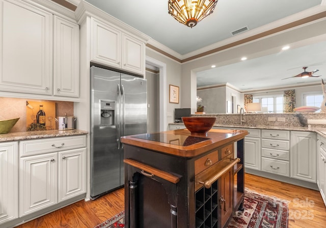 kitchen featuring stainless steel fridge, white cabinetry, crown molding, and light wood-style floors