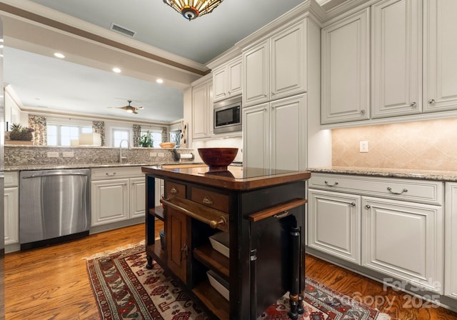 kitchen featuring visible vents, crown molding, decorative backsplash, wood finished floors, and stainless steel appliances