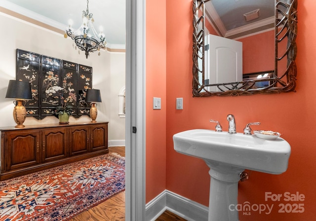 bathroom with a notable chandelier, wood finished floors, baseboards, and ornamental molding