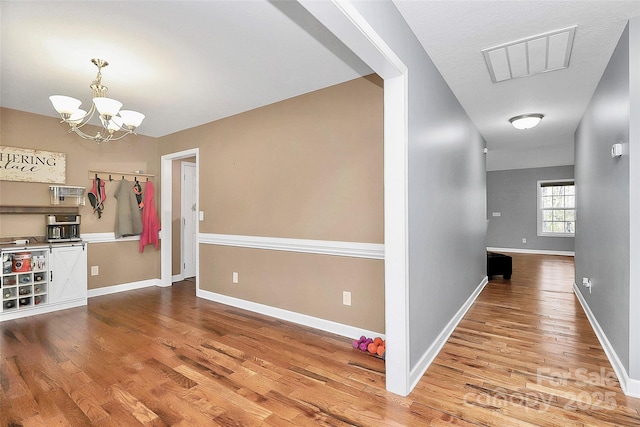 hallway featuring an inviting chandelier, wood finished floors, visible vents, and baseboards